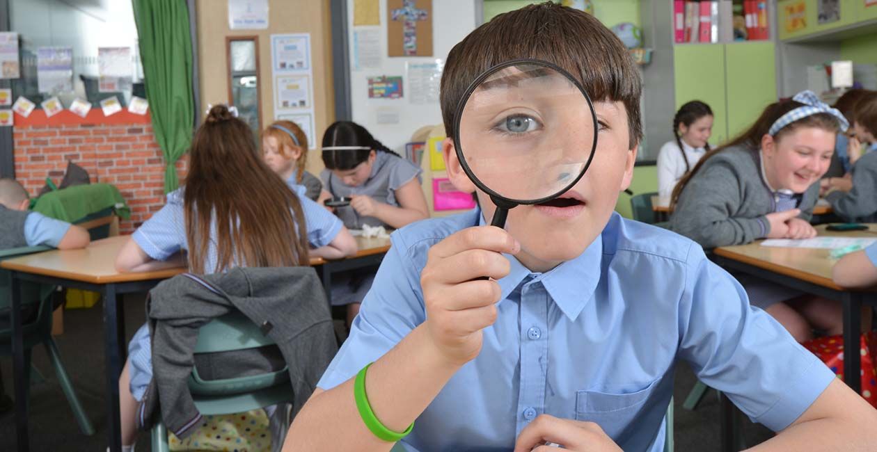 Boy in classroom looking through a magnifying glass